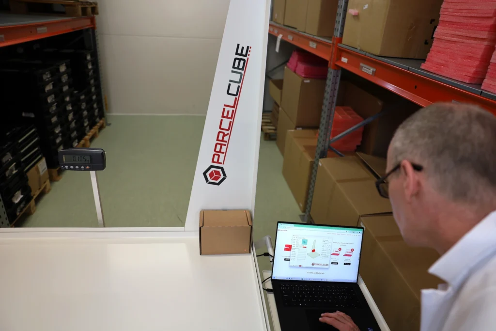 Varastotyöntekijä mittaamassa pakettia Parcelcube 1000 -mittausjärjestelmällä ja helppokäyttöisellä ohjelmistolla.